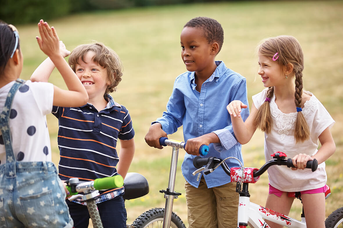 Vier Kinder mit unterschiedlichen Hautfarben mit dem Fahrrad und Cityroller geben sich High-Five