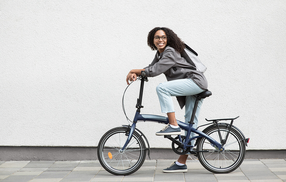 Junge Frau sitzt lachend auf einem Fahrrad mit grauen Jacke, Jeans und einem Rucksack
