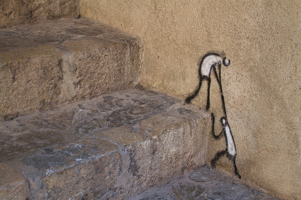 Steinstufen mit einer Malerei an der Wand von zwei Figuren. Die eine Figur zieht die andere die Stufen hoch.