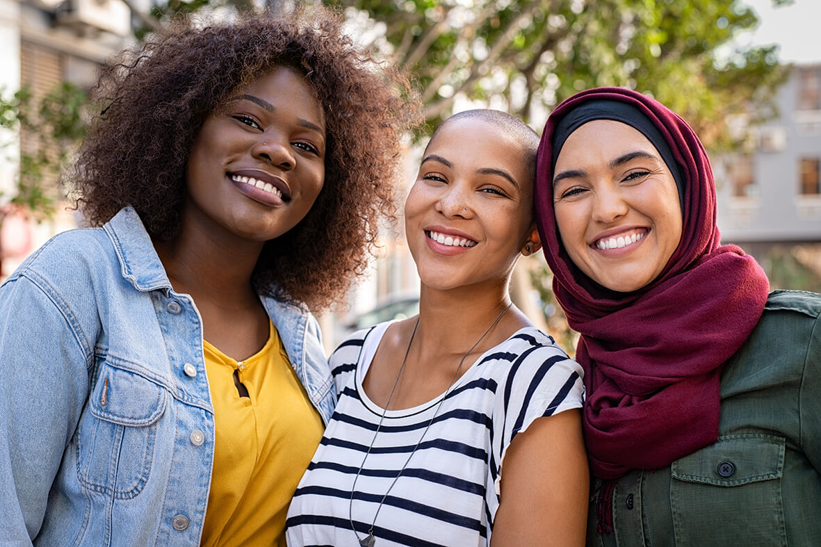 Drei junge Frauen mit verschiedenen Ethnien lachen in die Kamera