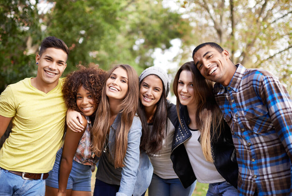 Eine Gruppe mit sechs Jugendlichen lachen Arm in Arm in die Kamera