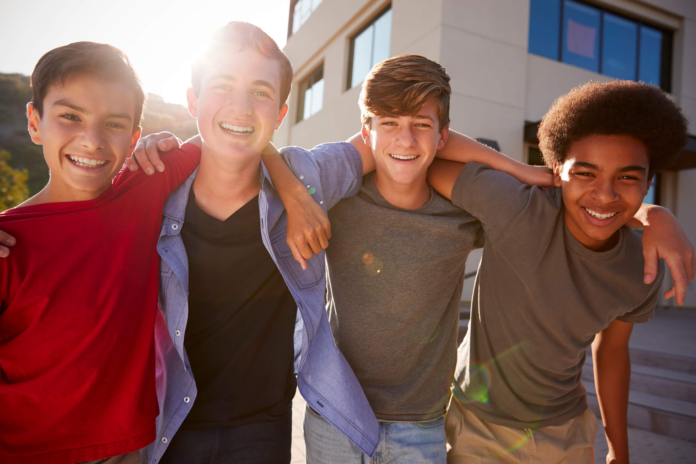 Vier Jungs Arm in Arm, lachen in die Kamera vor einem Gebäude.
