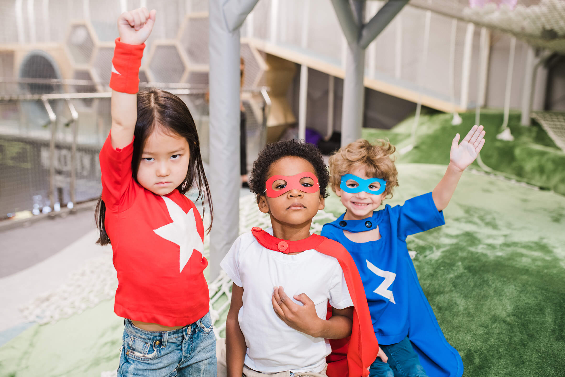 Ein Mädchen, zwei Jungs mit Superhelden Kostüm in blau und rot. Die Jungs haben Masken auf und das Mädchen macht die Superhelden Pose.